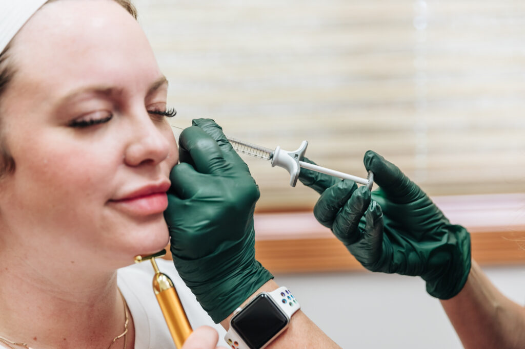 A provider wearing gloves and an Apple watch injects a smiling patient with Sculptra near Kalamazoo.